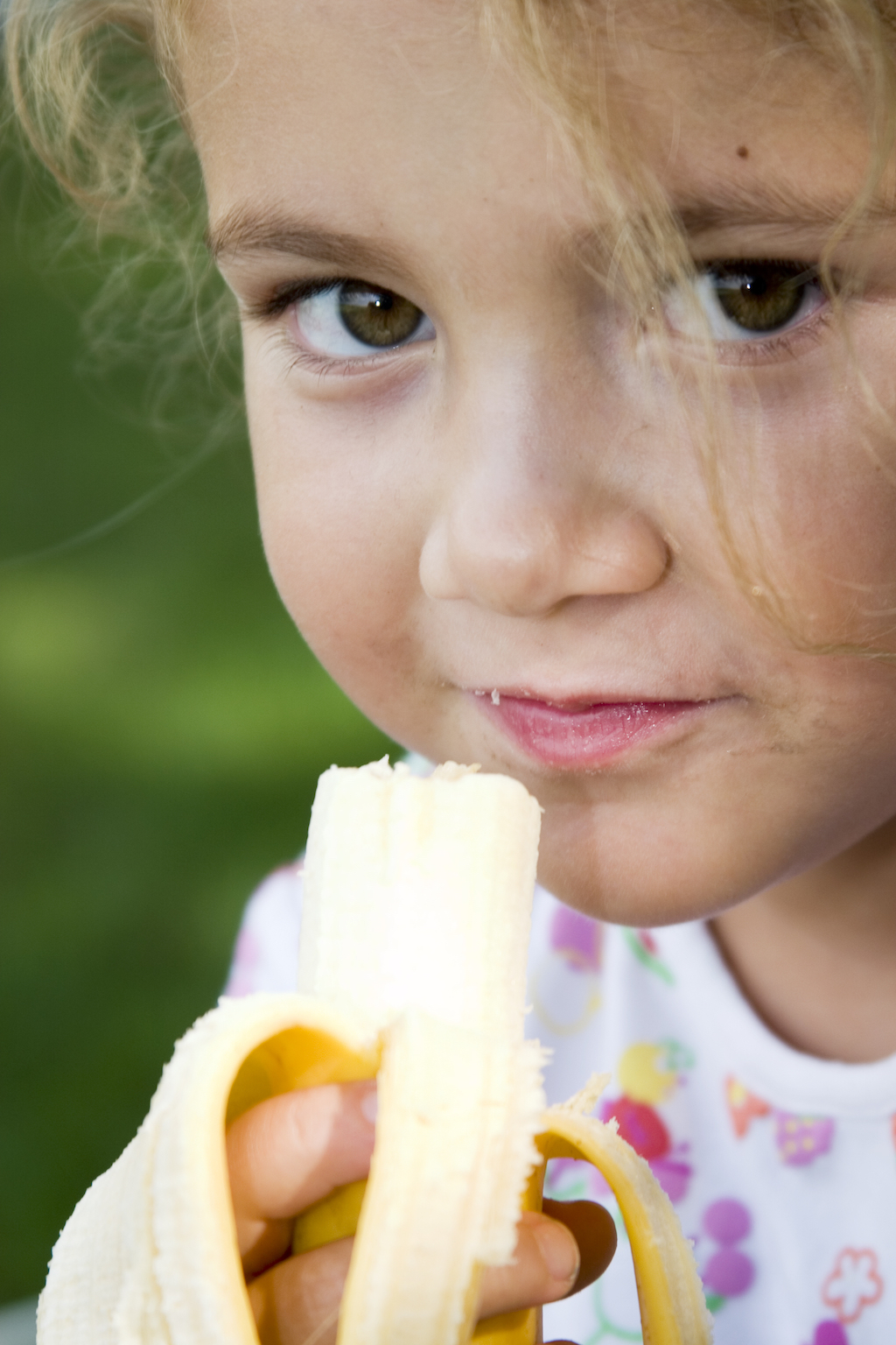 little girl eating a banana at the park